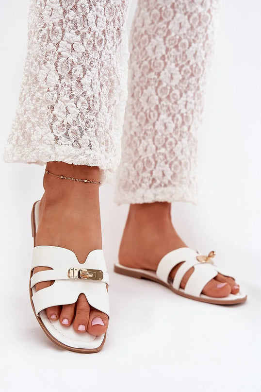 Sandales élégantes blanches inspirées de la culture brésilienne avec design ouvert, attache en métal sophistiquée, portées avec un pantalon en dentelle blanche, incarnant un style chic et tropical idéal pour l'été.