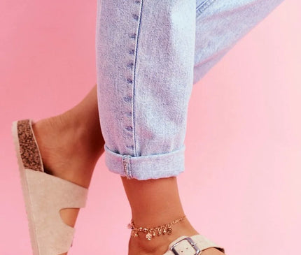 Sandales décontractées et élégantes inspirées du Brésil en daim beige avec deux boucles argentées, semelle en liège confortable, portées avec un jean retroussé sur fond rose, parfaites pour la plage ou une journée en ville.