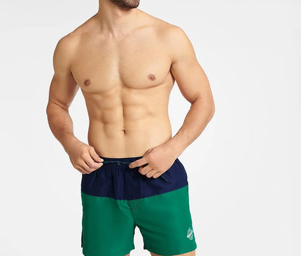 Homme souriant portant un maillot de bain GEM bicolore bleu marine et vert, conçu pour l'été et les activités nautiques, avec une coupe mi-cuisse, une taille élastique et un cordon de serrage. Le maillot arbore un emblème blanc sur le côté gauche avec le mot Summer.