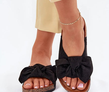 Sandales noires élégantes avec un nœud en velours, semelle en liège marron, évoquant l'artisanat et le style décontracté brésilien. Idéales pour les sorties estivales et une touche bohème, portées avec un pantalon beige et un bracelet de cheville doré.