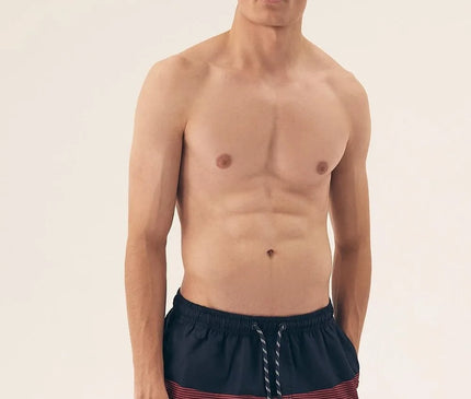 Homme portant un short de bain pour hommes rouge et noir à imprimé tendance, avec une taille élastique et des cordons ajustables. Modèle léger, à séchage rapide, avec une doublure intérieure pour plus de confort. Idéal pour la plage ou la piscine.