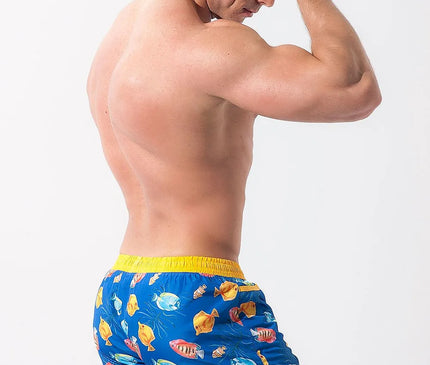 Short de bain Playo Fish en polyester 100 % bleu avec motif coloré de poissons tropicaux, bordé de passepoil jaune. Conçu pour un porté confortable, il possède une taille élastique avec cordon de serrage et une doublure en maille intérieure. Parfait pour la plage ou la baignade.