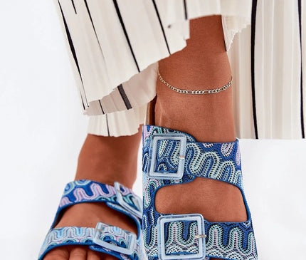 Sandales pour femmes à motifs colorés en textile, avec une plateforme en liège de 3 cm. Deux brides ajustables ornées de boucles décorées de paillettes, offrant confort et style. Semelle intérieure en cuir suédé naturel, parfaite pour les journées estivales. Présenté avec une jupe plissée blanche à rayures noires pour une tenue légère et élégante.