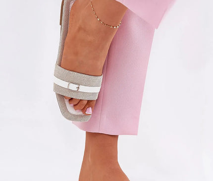 Sandales plates pour femmes en matériau textile avec une fine bride et une boucle, semelle de 1 cm, idéales pour l'été, portées avec un pantalon rose clair.