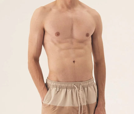 Homme portant un short de bain beige avec des motifs tropicaux subtils, inspiré du style décontracté et festif des plages brésiliennes, idéal pour une promenade en bord de mer ou un moment de détente.