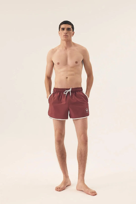 Short de bain homme couleur bordeaux, inspiré de l'énergie vibrante du littoral brésilien, avec bordures blanches, cordon ajustable et coupe courte évoquant l'élégance tropicale et le dynamisme brésilien. Parfait pour la plage, le sport ou des moments de détente en été.