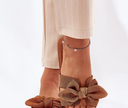 Sandales pour femmes en tissu couleur marron, ornées d'un nœud décoratif à l'avant. Confectionnées avec un talon plat de 1 cm, elles offrent un style estival confortable et élégant. Parfaites pour accompagner des robes d'été, jupes ou shorts. Présentées avec des pieds féminins et un pantalon beige pour illustrer leur look raffiné.