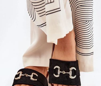 Claquettes en suédine écologique noires avec détail décoratif doré à l'avant, montées sur une plateforme ornée de paillettes, ajoutant une touche glamour. Semelle profilée pour un confort optimal, idéal pour les jours d'été et facile à associer aux robes, jupes ou pantalons.