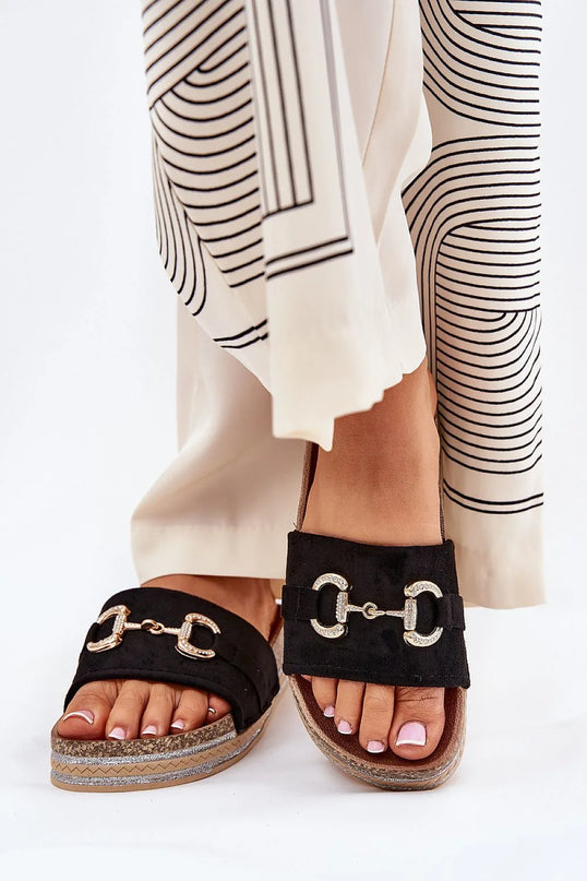 Claquettes en suédine écologique noires avec détail décoratif doré à l'avant, montées sur une plateforme ornée de paillettes, ajoutant une touche glamour. Semelle profilée pour un confort optimal, idéal pour les jours d'été et facile à associer aux robes, jupes ou pantalons.