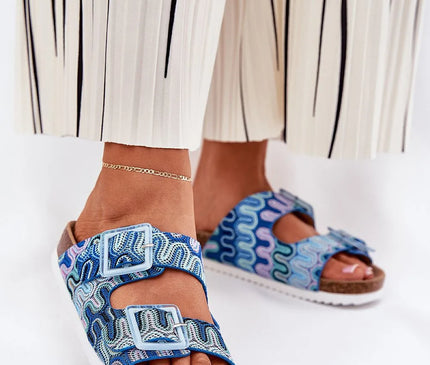 Sandales pour femmes sur plateforme en liège, avec motifs colorés en tissu textile, deux brides à boucles décorées de paillettes, semelle intérieure en cuir suédé, parfaites pour l'été. Présentées portées avec un pantalon blanc à rayures noires.