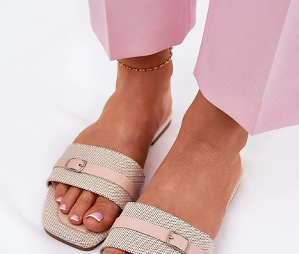 Sandales plates pour femmes en tissu textile beige, avec une bride ornée d'une boucle argentée sur l'avant. Semelle confortable en cuir écologique et tissu, talon plat de 1 cm. Idéales pour les journées chaudes, assorties à des pantalons roses pour un look estival.