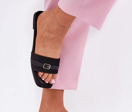 Sandales plates pour femmes en matériau textile noir, dotées d'une fine bride avec boucle décorative à l'avant, portées avec un pantalon rose. Idéales pour l'été, elles offrent confort et style avec une semelle de 1 cm en cuir écologique et tissu, parfaites pour les tenues légères.