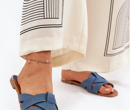 Sandales plates pour femmes en tissu textile bleu avec des brides entrelacées à l'avant, design élégant et simple, idéales pour l'été. Portées avec un pantalon fluide à motifs, mettant en valeur leur style décontracté et raffiné.