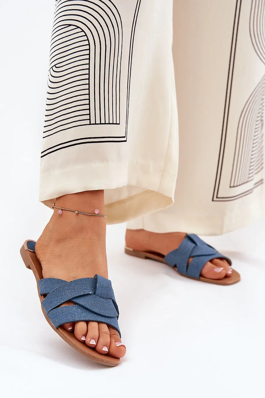 Sandales plates pour femmes en tissu textile bleu avec des brides entrelacées à l'avant, design élégant et simple, idéales pour l'été. Portées avec un pantalon fluide à motifs, mettant en valeur leur style décontracté et raffiné.