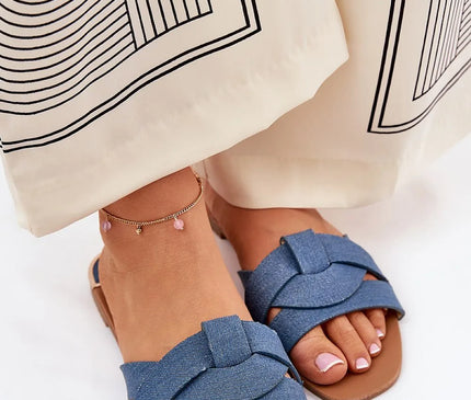 Sandales plates pour femmes en tissu textile bleu avec des brides entrelacées à l'avant, semelle de 1 cm en cuir artificiel, portées avec un pantalon beige décoré de motifs géométriques noirs, offrant un style élégant et confortable.