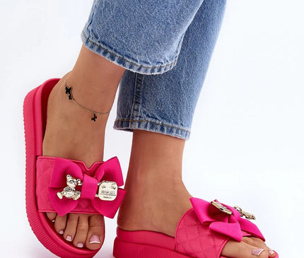 Mules pour femmes en simili cuir rose vif avec plateforme massive de 4,5 cm. Décorées d'un grand nœud en tissu, d'un fermoir imitation avec un motif d'ours en peluche et une plaque métallique à inscription. Parfaites pour un style audacieux et estival.