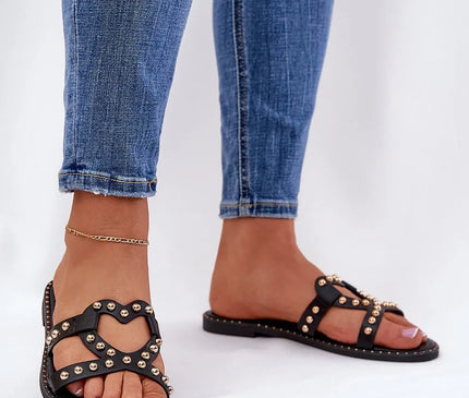 Sandales femme noires inspirées de la mode brésilienne, ornées de détails métalliques dorés et au design audacieux, évoquant l'esprit festif des plages du Brésil. Idéales pour les promenades estivales avec une touche élégante et décontractée, portées ici avec un jean ajusté.