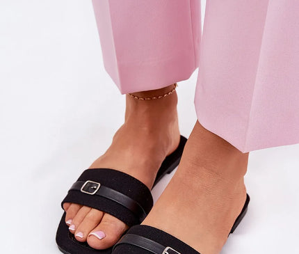Sandales plates pour femmes en tissu noir avec une fine bride décorative et boucle, semelle confortable en cuir écologique et tissu. Parfaites pour l'été, elles sont combinées ici avec un pantalon rose clair.