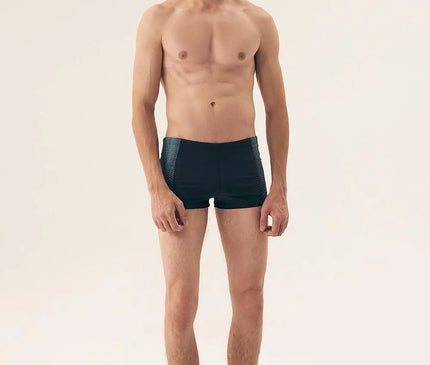 Homme portant un maillot de bain masculin moderne et minimaliste, inspiré par le style décontracté des plages brésiliennes comme Copacabana et Ipanema. Maillot noir ajusté avec un design élégant, parfait pour allier confort et allure.