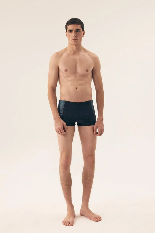 Homme portant un maillot de bain masculin moderne et minimaliste, inspiré par le style décontracté des plages brésiliennes comme Copacabana et Ipanema. Maillot noir ajusté avec un design élégant, parfait pour allier confort et allure.