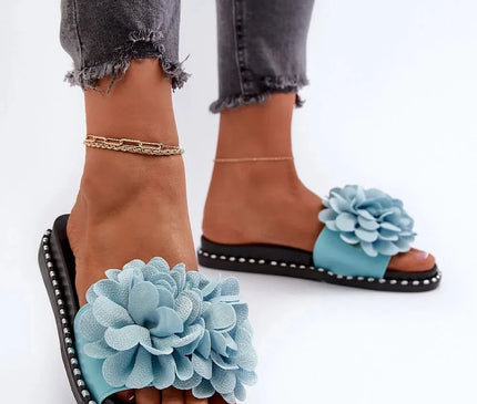 Claquettes pour femmes avec une décoration florale frappante en bleu sur le devant, semelle en caoutchouc de 2,5 cm rehaussée de détails décoratifs blancs. Idéales pour les journées chaudes, elles représentent une coupe classique et élégante, parfaites pour un style décontracté et estival.