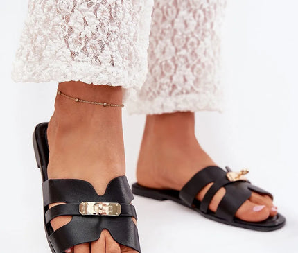 Sandales noires élégantes et sophistiquées avec détails en métal doré, inspirées du style brésilien, portées avec un pantalon en dentelle blanche. Design minimaliste et raffiné, parfait pour un look naturel et ensoleillé.