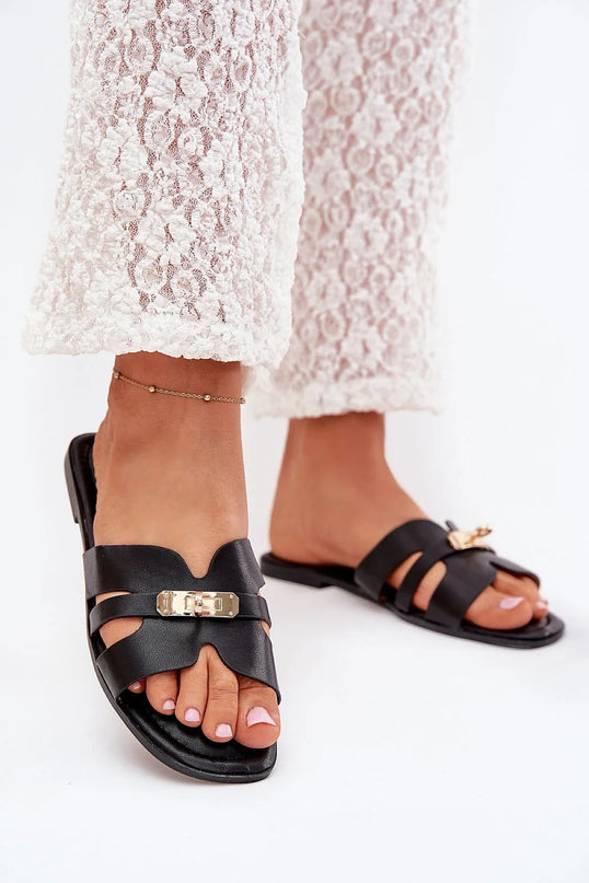 Sandales noires élégantes et sophistiquées avec détails en métal doré, inspirées du style brésilien, portées avec un pantalon en dentelle blanche. Design minimaliste et raffiné, parfait pour un look naturel et ensoleillé.