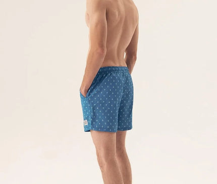 Homme vêtu d'un maillot de bain bleu à motifs marins, inspiré de l'élégance et de l'énergie des plages brésiliennes. Le short symbolise le lifestyle tropical avec un équilibre parfait entre confort et esthétique, idéal pour une journée en bord de mer ou une promenade sur la plage.
