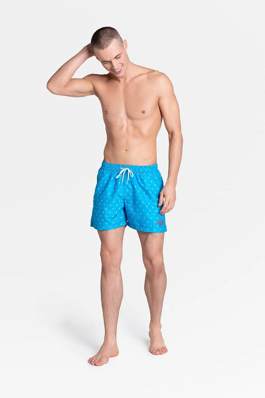 Short de bain ample et doublé pour homme, couleur bleue avec un motif discret, équipé d'une ceinture élastique ajustable avec cordon de serrage, tissu à séchage rapide, présenté par un mannequin, collection été 2021 Henderson.