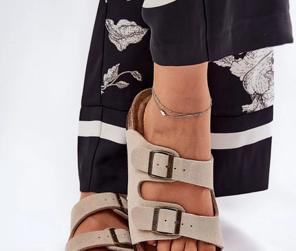 Sandales élégantes à double bride beige avec boucles métalliques, inspirées du style décontracté et chic du Brésil. Parfaites pour les promenades à la plage ou les sorties estivales, ces sandales allient confort et esprit de liberté, mises en avant avec une tenue tendance à motifs noirs et blancs.
