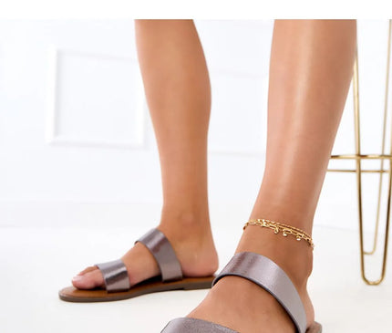 Sandales minimalistes à deux brides larges en finition métallisée, inspirées du style brésilien chic et décontracté, parfaites pour les journées ensoleillées ou les soirées estivales. Élégance et confort avec une semelle plate adaptée à un mode de vie dynamique et relax. Accessoire idéal pour évoquer l'esprit des plages et rues animées du Brésil.