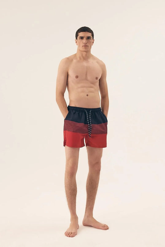 Homme portant un short de bain rouge et noir avec cordons de serrage, à imprimé tendance, fabriqué en polyester léger et à séchage rapide, idéal pour la plage ou la piscine.