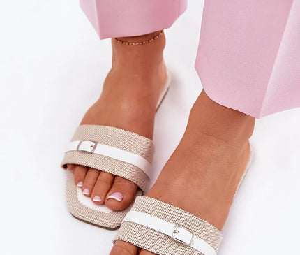 Sandales plates pour femmes en tissu beige avec bride fine à boucle blanche sur l'avant. Élégantes et confortables, parfaites pour des tenues d'été légères. Portées ici avec un pantalon rose pastel pour un look estival et chic.