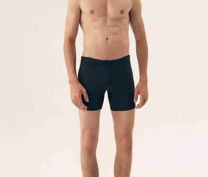 Homme portant un short de bain noir minimaliste et élégant pour homme, conçu avec une longueur de jambe moyenne. Le short est fabriqué en tissu lisse et à séchage rapide, idéal pour la plage ou les activités aquatiques. Modèle sans poches, avec taille à lacets pour un ajustement parfait, photographié sur un fond neutre.