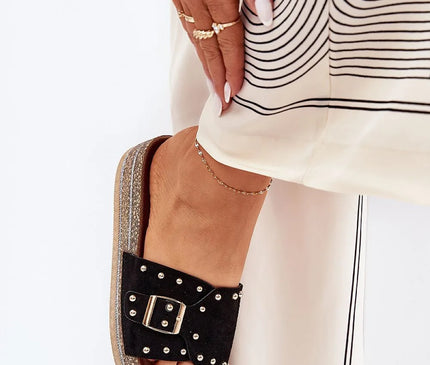 Sandales inspirées de l'artisanat brésilien avec des décorations métalliques, semelle compensée texturée et bride noire ornée d'une boucle argentée, portées avec une tenue chic pour un style estival et élégant.