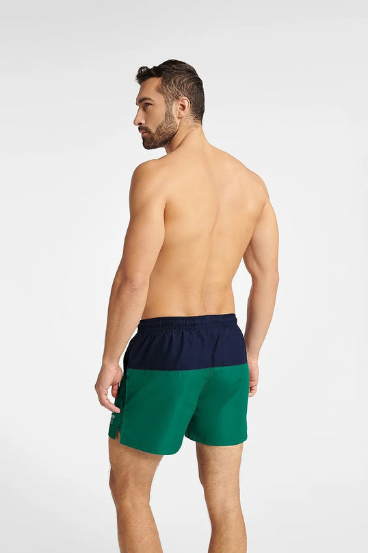 Homme de dos portant un maillot de bain GEM bicolore vert et bleu marine, taille mi-cuisse avec taille élastiquée et cordon de serrage, idéal pour les sports nautiques et l'été, avec petite ouverture sur les côtés pour une meilleure liberté de mouvement.