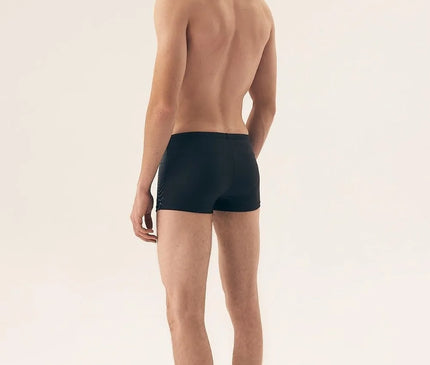 Homme portant un maillot de bain moderne et minimaliste noir, inspiré de l'élégance décontractée des plages brésiliennes telles que Copacabana et Ipanema, mettant en valeur le confort et le style.