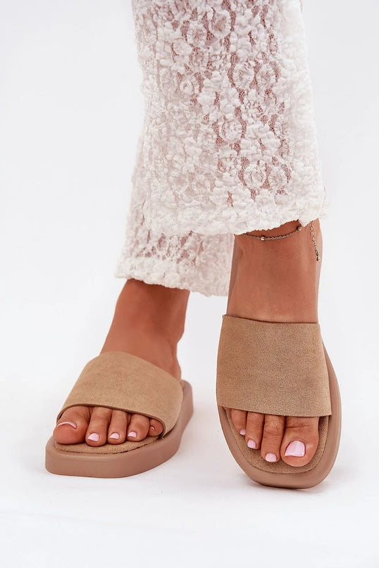 Sandales minimalistes beige pour femmes, inspirées du style décontracté et tropical du Brésil, avec une large sangle en matière légère et confortable, idéales pour les journées estivales ou une tenue chic et décontractée. Portées avec un pantalon en dentelle blanche.