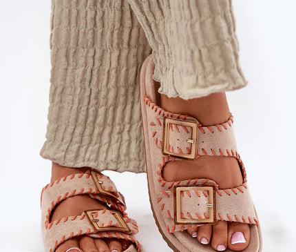 Sandales artisanales inspirées du Brésil avec coutures apparentes orange et boucles dorées, parfaites pour un style élégant et décontracté, portées avec un pantalon beige texturé.