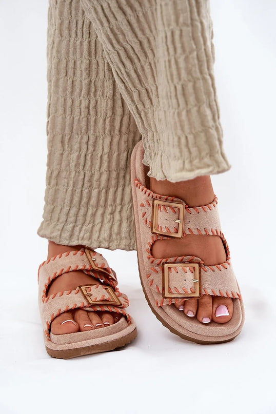 Sandales artisanales inspirées du Brésil avec coutures apparentes orange et boucles dorées, parfaites pour un style élégant et décontracté, portées avec un pantalon beige texturé.