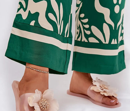 Sandales glamour roses avec une grande fleur exotique en décoration, inspirées des paysages tropicaux brésiliens. Idéales pour un style estival élégant, associées à un pantalon vert à motifs tropicaux. Parfaites pour une promenade ou une soirée en bord de mer.