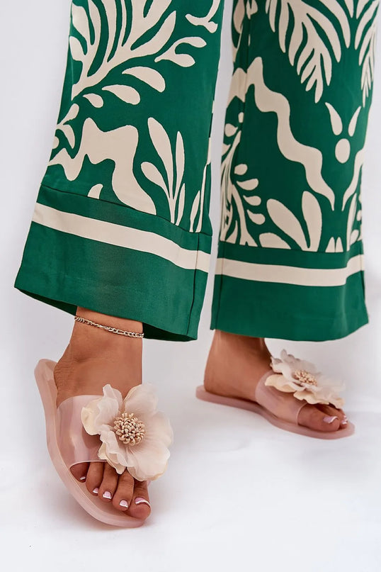 Sandales glamour roses avec une grande fleur exotique en décoration, inspirées des paysages tropicaux brésiliens. Idéales pour un style estival élégant, associées à un pantalon vert à motifs tropicaux. Parfaites pour une promenade ou une soirée en bord de mer.