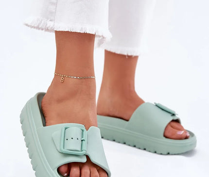 Claquettes pour femmes en mousse vert menthe avec plateforme de 4 cm, boucle décorative et sangle réglable pour ajustement. Idéales pour la piscine, les vacances ou des journées décontractées, portées avec un pantalon blanc à ourlet effiloché.
