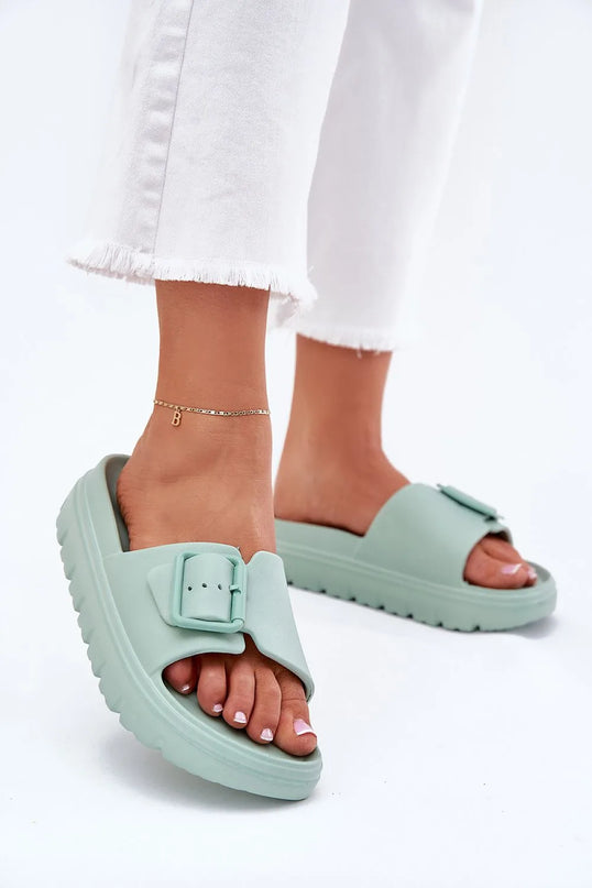 Claquettes pour femmes en mousse vert menthe avec plateforme de 4 cm, boucle décorative et sangle réglable pour ajustement. Idéales pour la piscine, les vacances ou des journées décontractées, portées avec un pantalon blanc à ourlet effiloché.