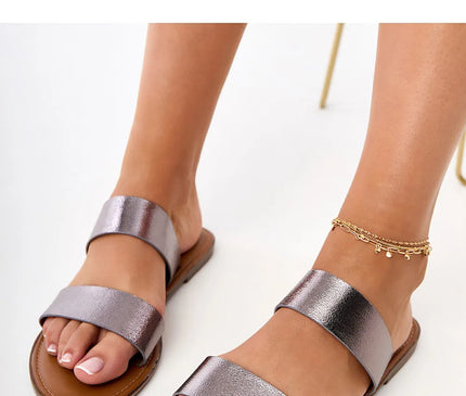 Sandales minimalistes et élégantes à brides larges en métal brillant, inspirées du style brésilien tropical, parfaites pour une promenade sur la plage ou une soirée décontractée. Confortables et légères, avec une semelle marron et un design chic rappelant l'art de vivre de Rio.