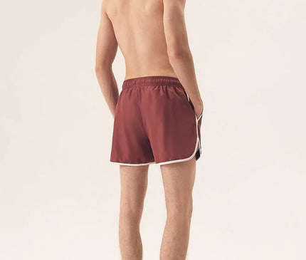 Short de bain homme de couleur bordeaux avec bordures blanches, inspiré par l'énergie et le style décontracté du littoral brésilien, idéal pour des journées ensoleillées à la plage comme à Copacabana. Confortable, moderne et polyvalent, conçu pour l'élégance estivale et le dynamisme tropical.