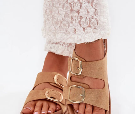 Sandales beige en imitation daim avec boucles dorées élégantes, inspirées de l'élégance décontractée brésilienne, portées avec un pantalon en dentelle blanche, idéales pour un look estival mêlant confort et style tropical.