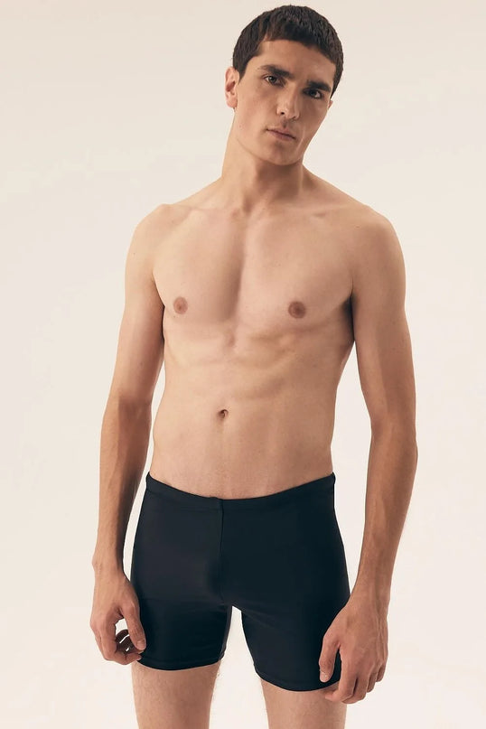 Shorts de bain noirs pour hommes avec une coupe ajustée et minimaliste, fabriqués en tissu à séchage rapide, présenté sur un modèle. Idéal pour la plage et les activités aquatiques. Longueur au-dessus de la mi-cuisse, conçu pour le confort et la liberté de mouvement, sans poches, avec une taille ajustable à lacets.