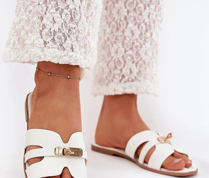 Sandales élégantes blanches inspirées de la culture brésilienne avec design ouvert, attache en métal sophistiquée, portées avec un pantalon en dentelle blanche, incarnant un style chic et tropical idéal pour l'été.