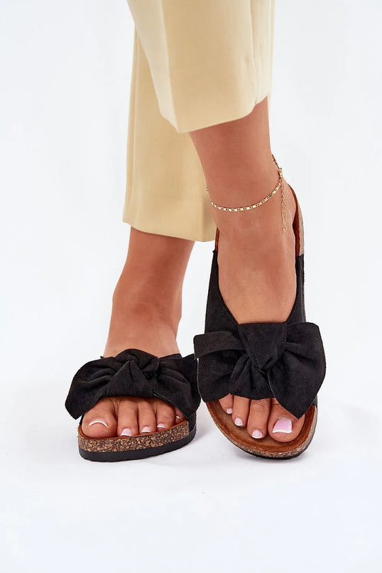 Sandales noires élégantes avec un nœud en velours, semelle en liège marron, évoquant l'artisanat et le style décontracté brésilien. Idéales pour les sorties estivales et une touche bohème, portées avec un pantalon beige et un bracelet de cheville doré.